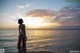 A woman standing in the water at sunset.